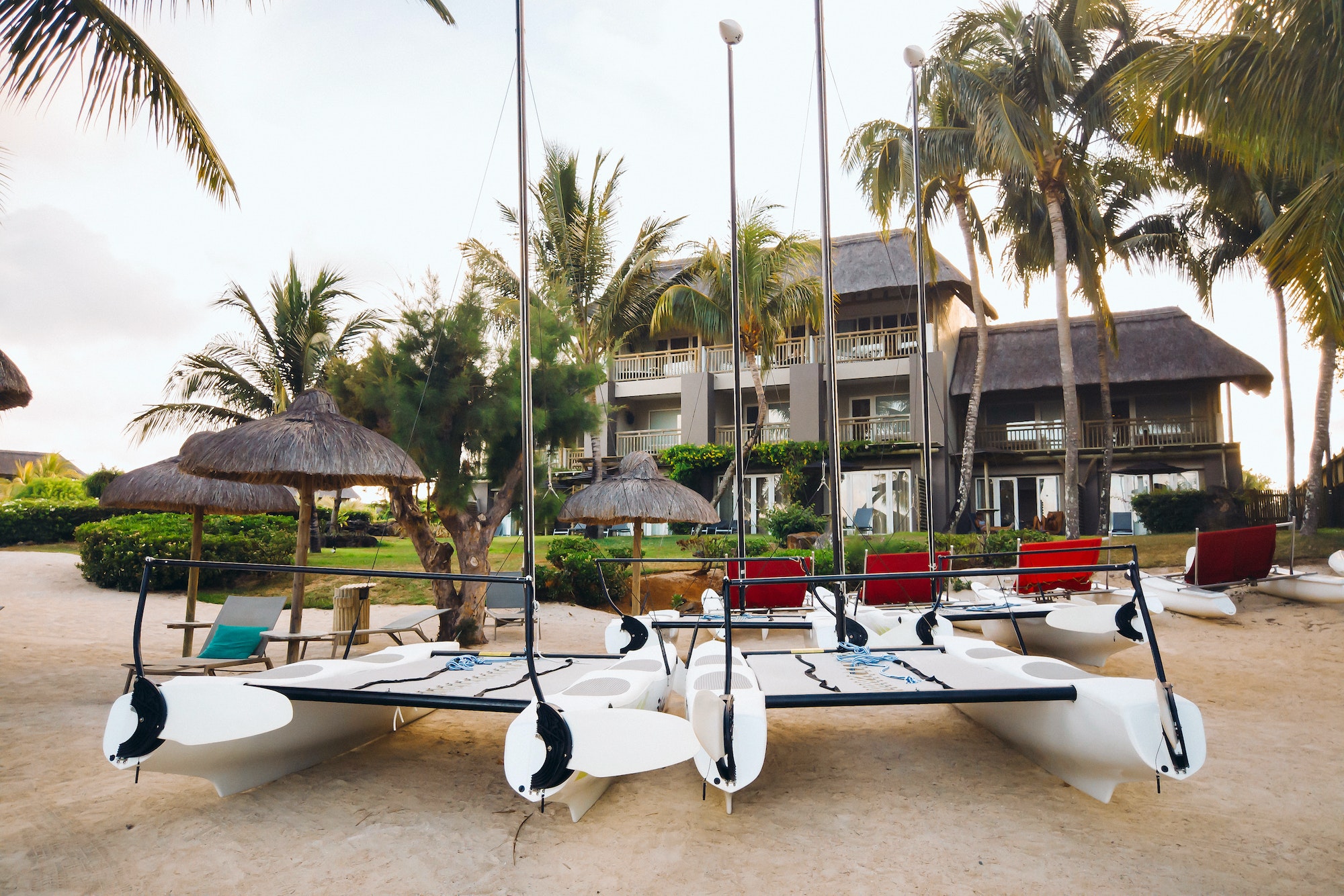 catamarans with sails are parked on the beach in front of a villa on the tropical island of