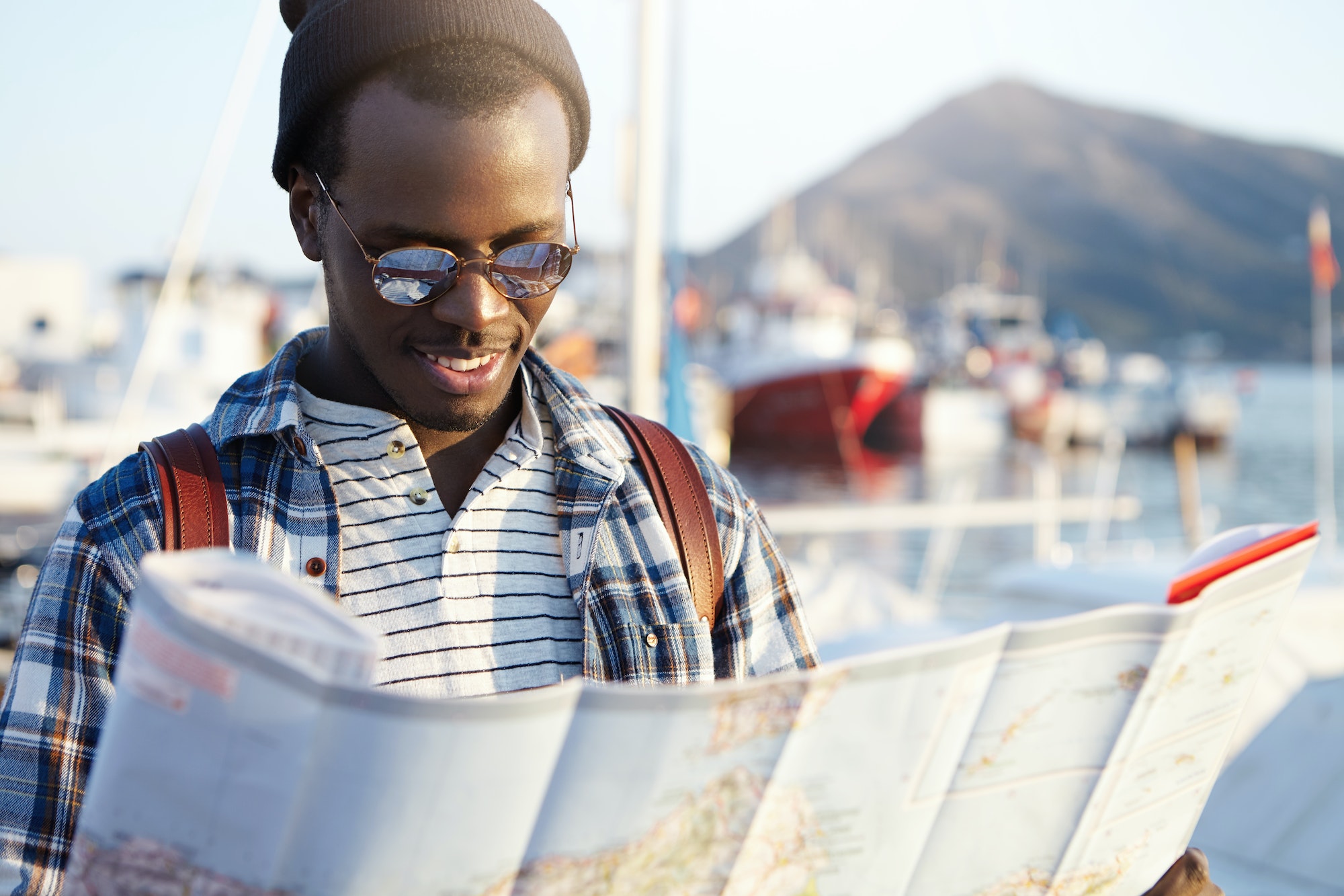 Happy excited dark-skinned man traveler wearing stylish clothing holding city guide in his hands whi